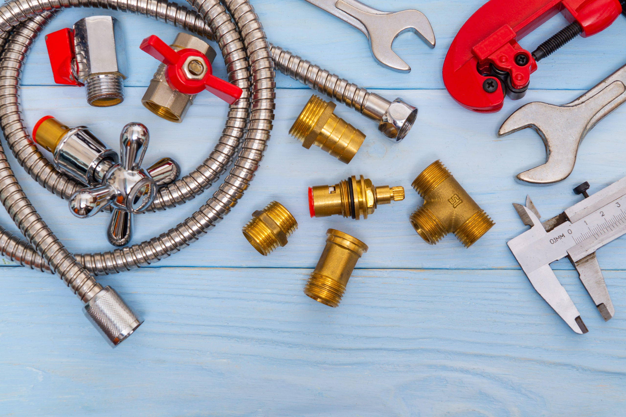 Necessary set of tools and spare parts for plumbers on blue wooden background.
